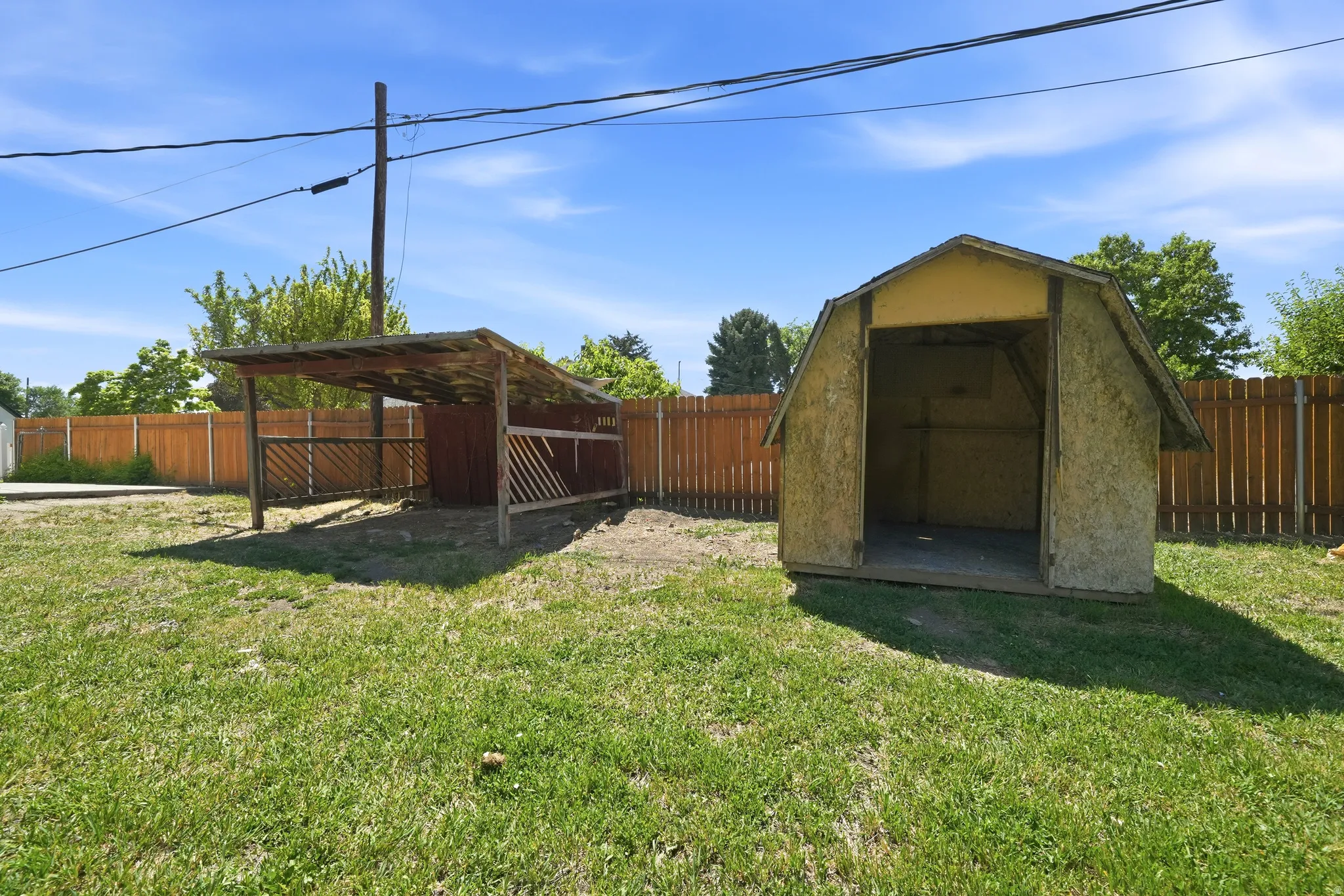 Expansive grassy yard featuring a wood privacy fence, a covered open-sided structure with wood fencing, and an additional storage shed