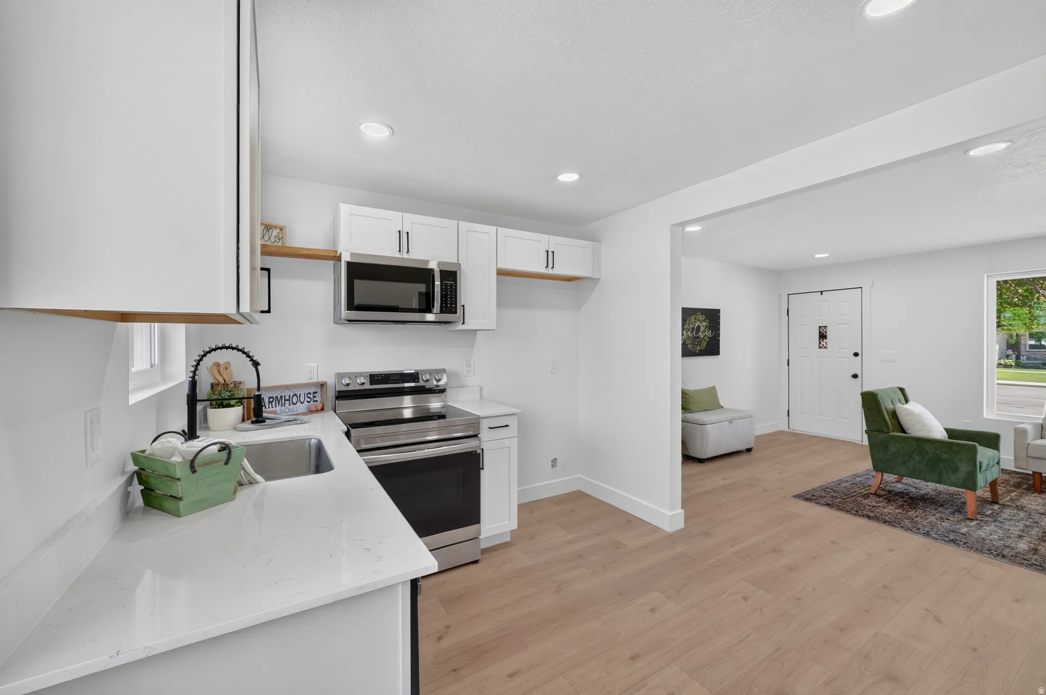 Bright kitchen featuring white cabinetry, light countertops, stainless steel appliances, and wood-finish flooring