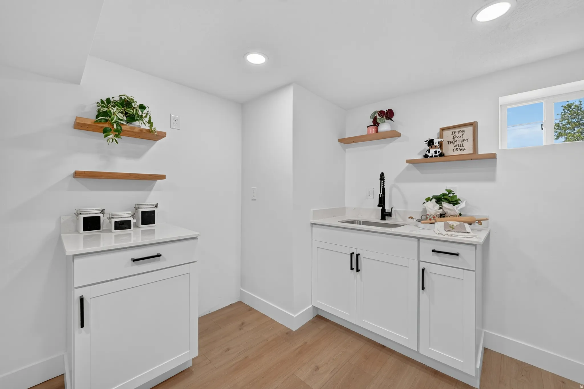 Dedicated utility space featuring a built-in sink with a matte black faucet, white cabinetry, and light wood-finish flooring