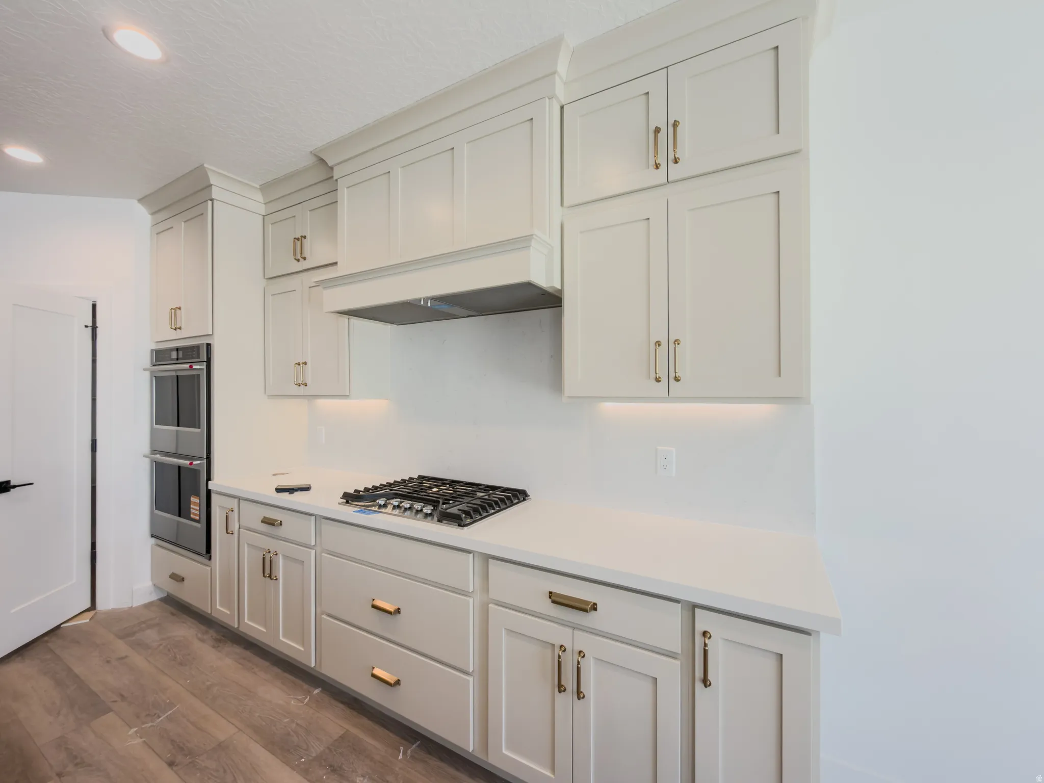 Kitchen featuring light-toned cabinetry with brass hardware, a built-in double oven, and a gas cooktop with a range hood