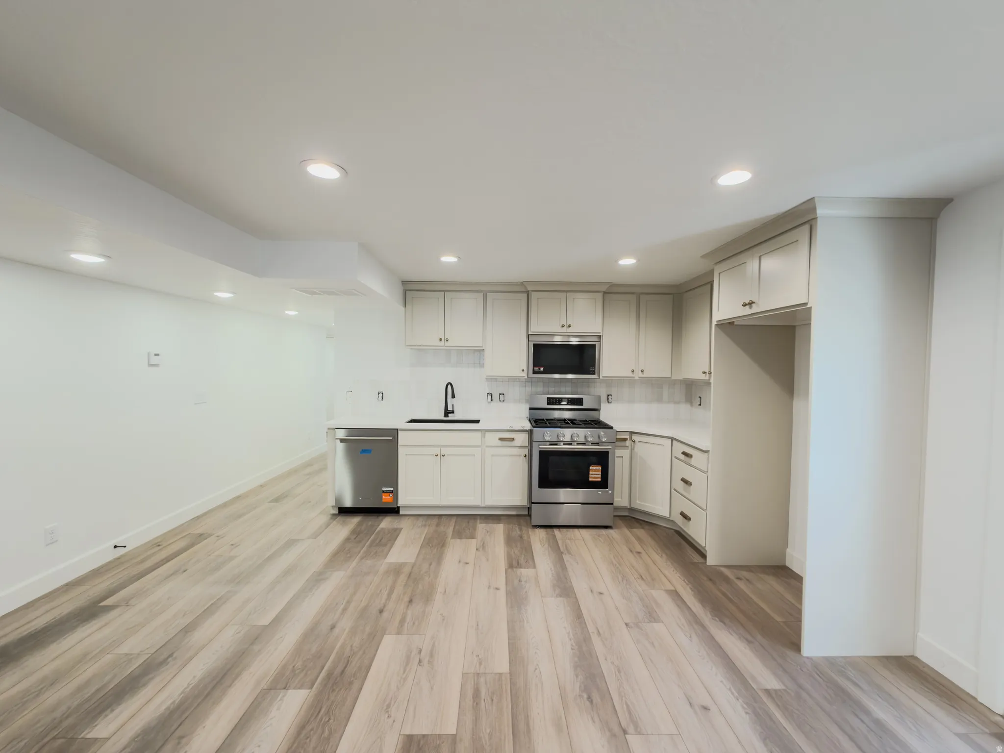 Open-concept kitchen with stainless steel appliances, white cabinetry, solid surface countertops, and wood-finish flooring