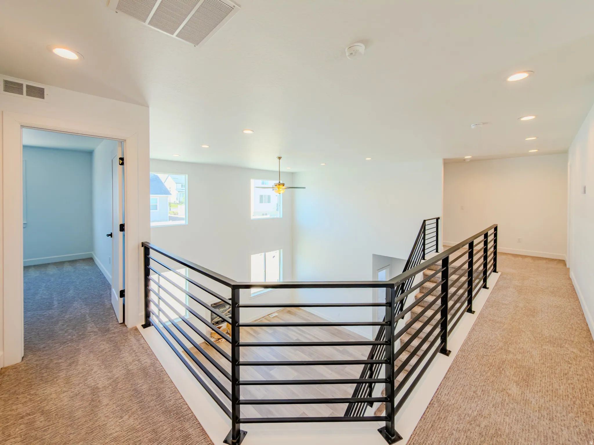 Upper-level landing featuring modern metal railings, recessed lighting, carpeted flooring, and a ceiling fan over the lower level