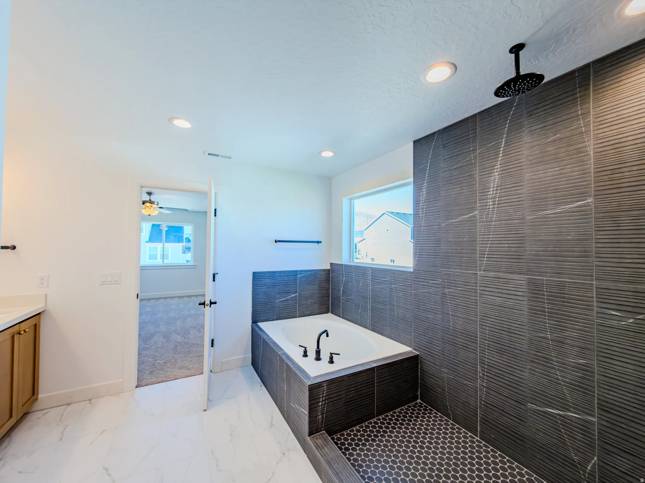 Modern bathroom featuring a built-in tub, a rainfall showerhead, and dark textured tile