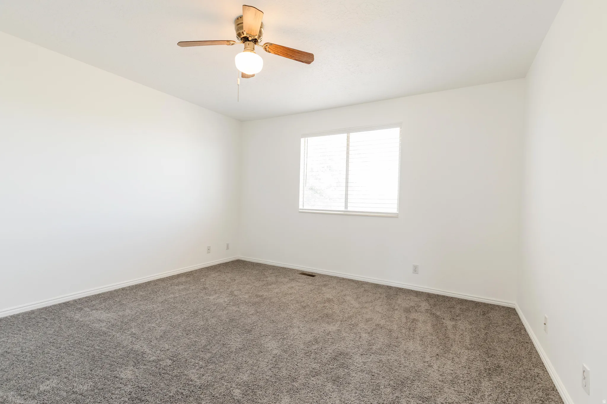Spacious room featuring neutral carpet flooring, white painted walls, a window with horizontal blinds, and a ceiling fan with integrated lighting