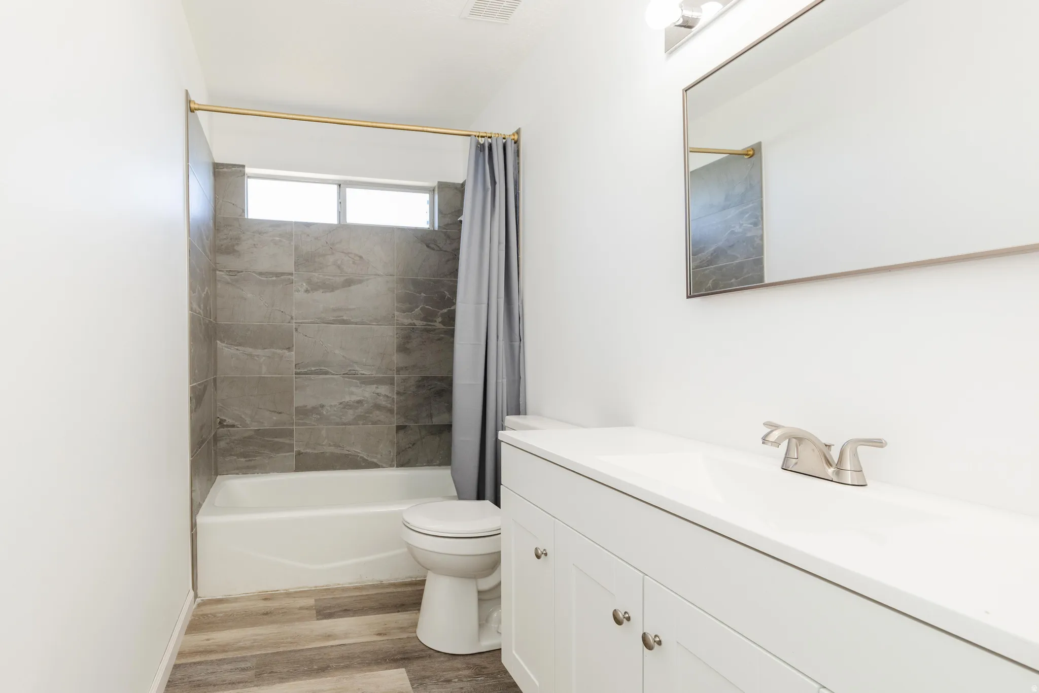 Bathroom featuring a white vanity with integrated sink, brushed nickel faucet, large mirror, and overhead lighting