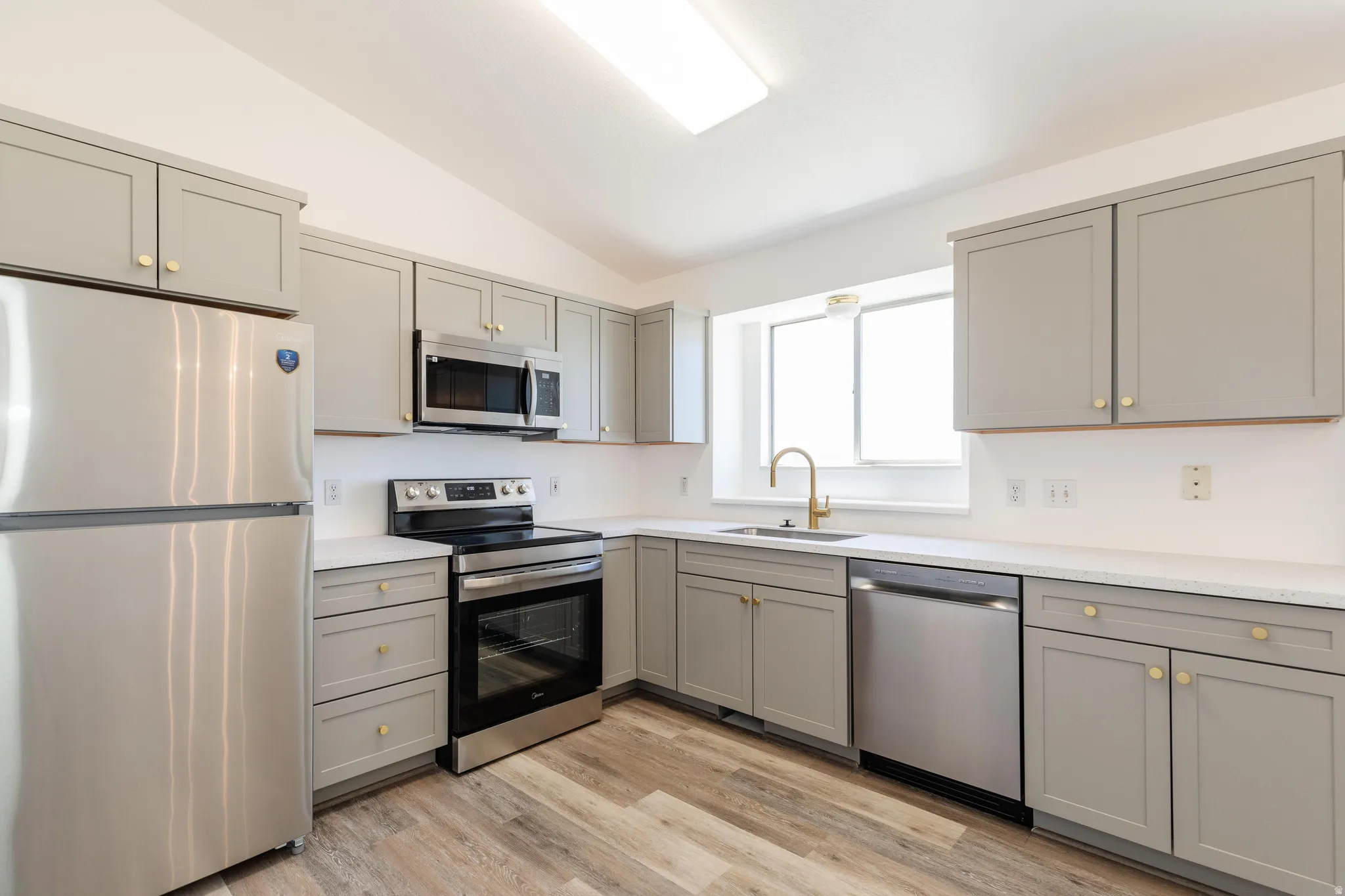 Kitchen featuring light gray cabinetry with gold-tone hardware, stainless steel appliances, white countertops, and wood-finish flooring