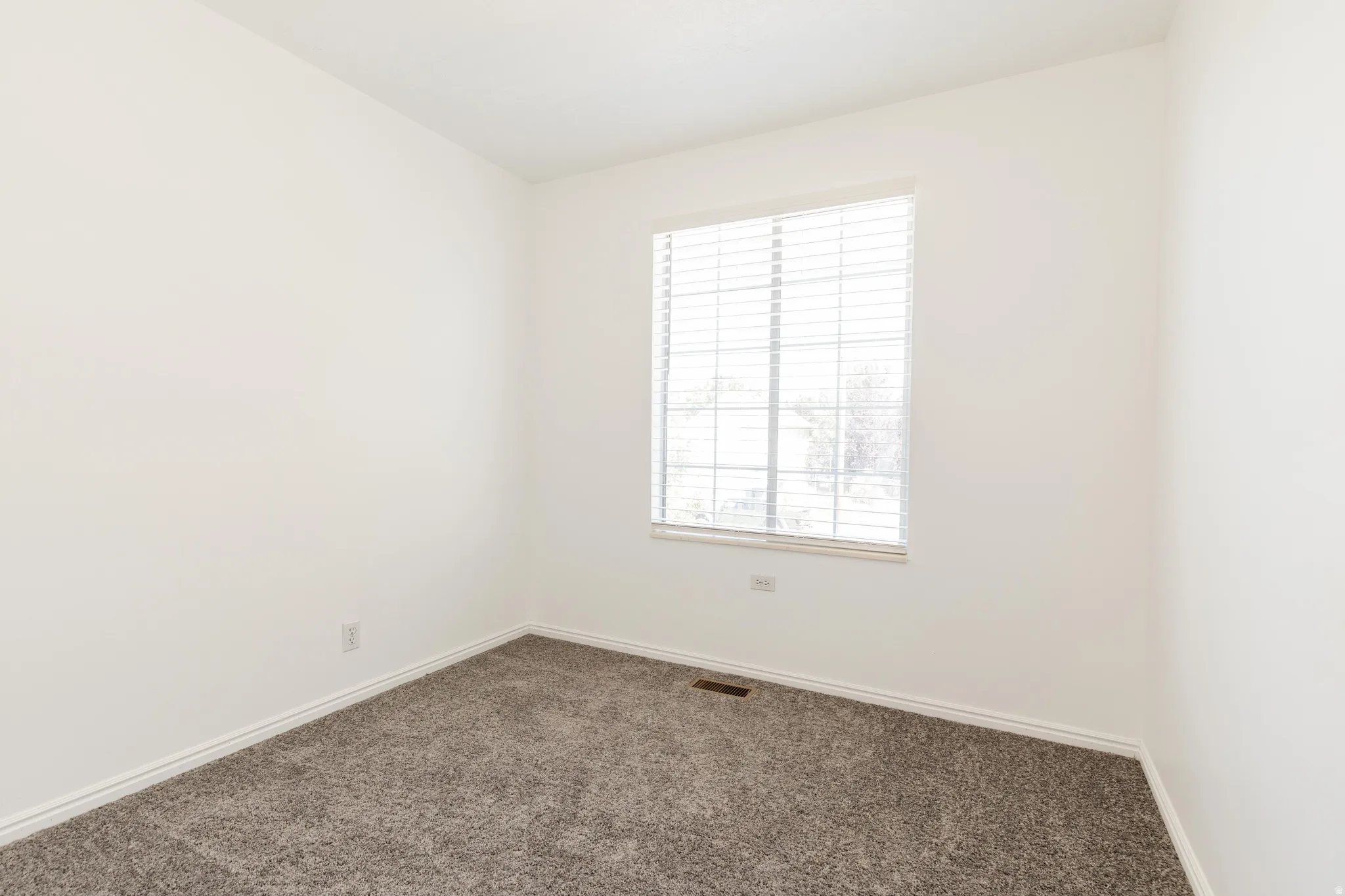 Bright room featuring neutral-toned walls, gray carpeting, and a window with horizontal blinds