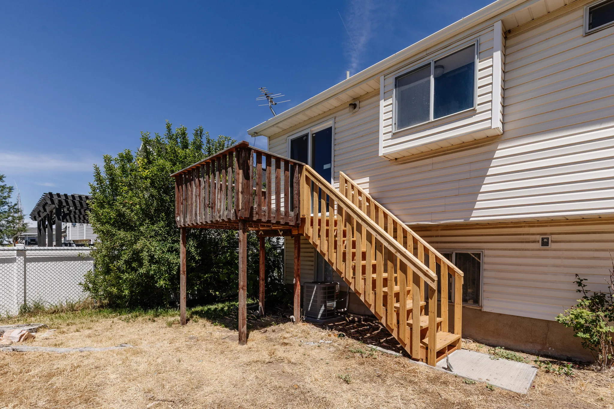 Property exterior featuring light-colored vinyl siding, a two-story wooden deck, and a newly constructed wooden staircase providing access to the yard