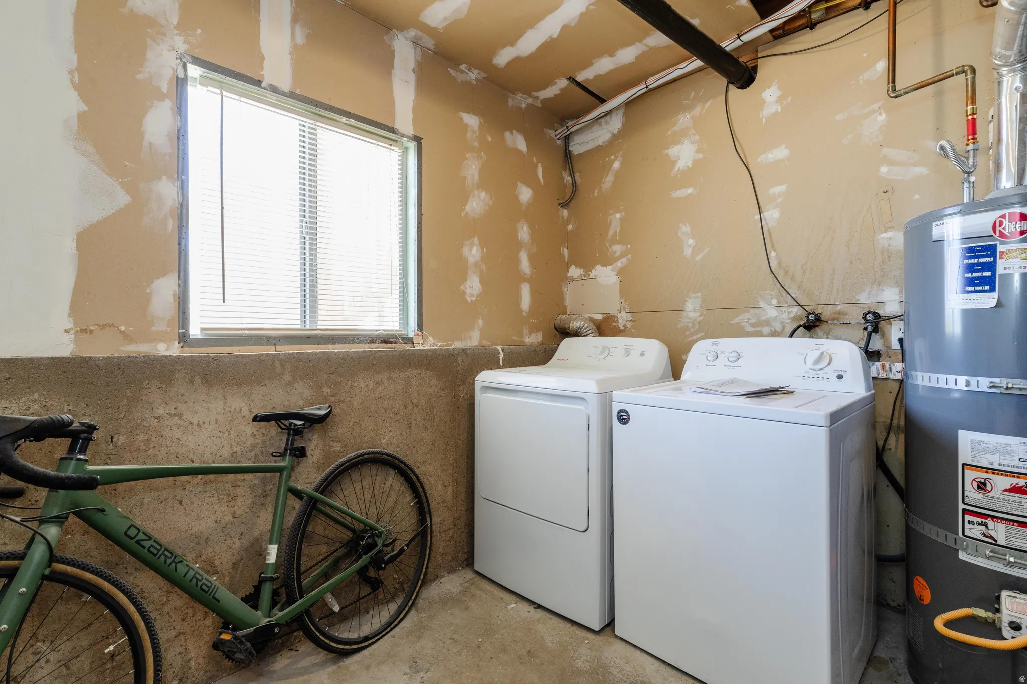 Laundry area featuring a window with blinds, exposed piping, and a water heater