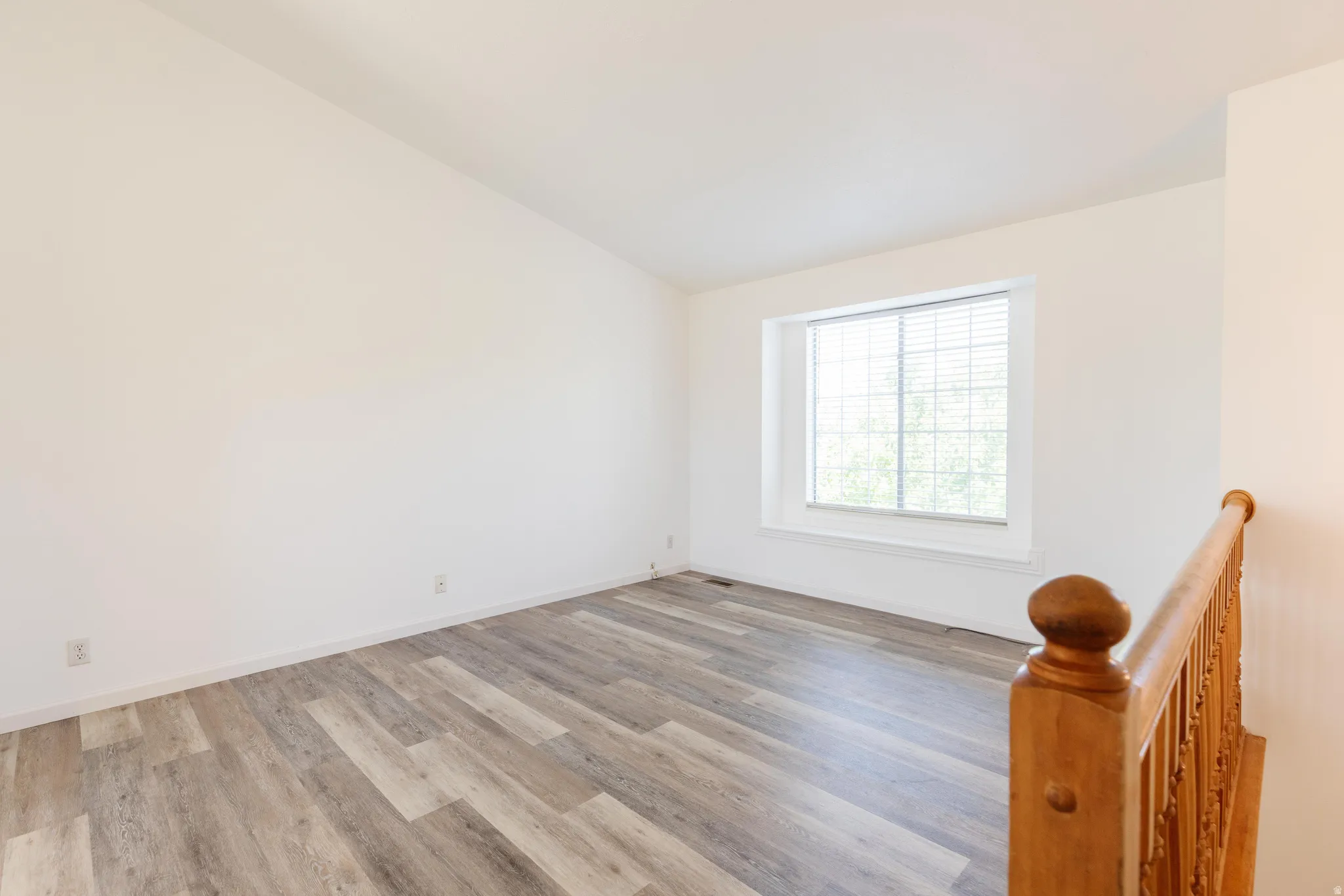 Bright interior space featuring wood-finish flooring, white baseboards, and a window with blinds