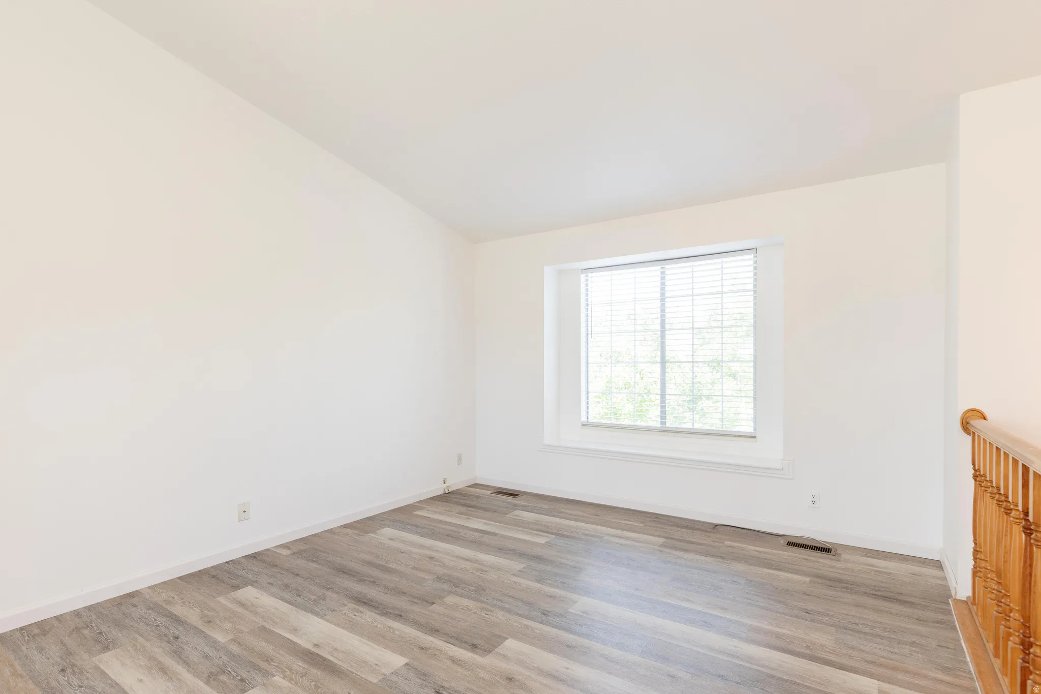 Spacious room with wood-finish flooring and a single window featuring horizontal blinds