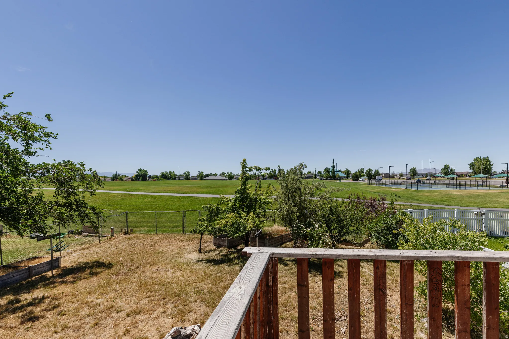 Outdoor deck with wood railing overlooking a sloped yard with established trees and raised garden beds