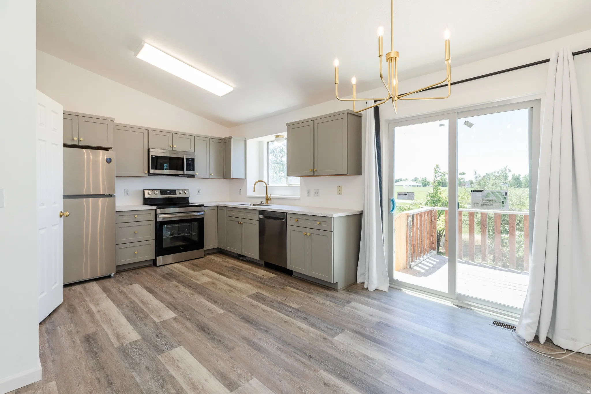 Open-concept kitchen and dining area featuring LVP flooring, gray shaker cabinetry, stainless steel appliances, white countertops, and a sliding glass door to a deck