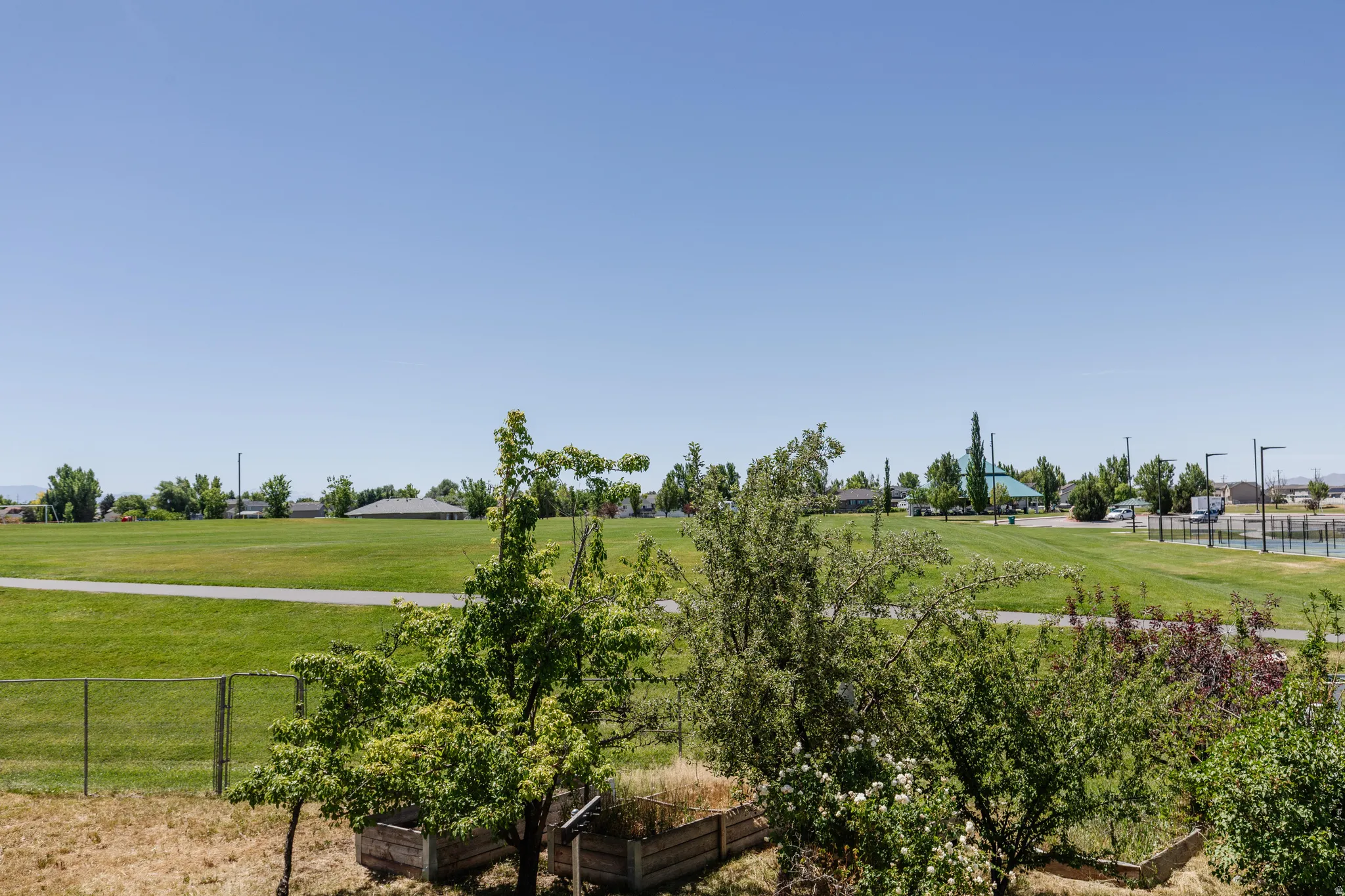 Expansive green space featuring a paved walking path, mature trees, and distant recreational facilities