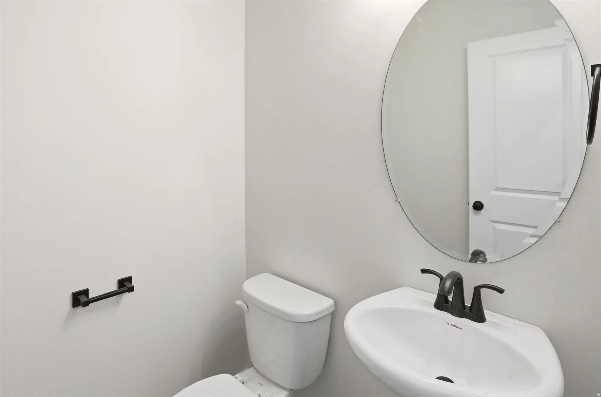 Pedestal sink with dark bronze fixtures and an oval frameless mirror