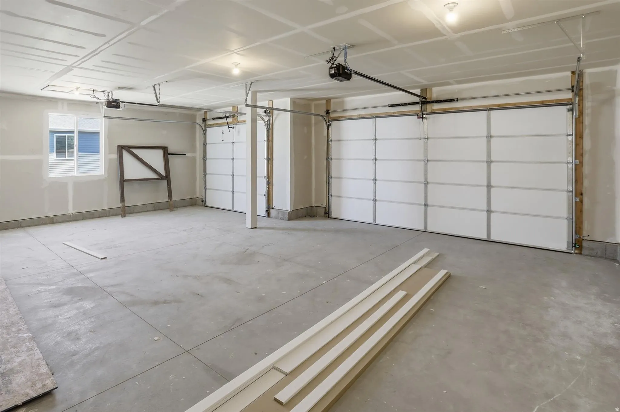 Spacious garage featuring two overhead doors, concrete flooring, overhead lighting, and a prominent window