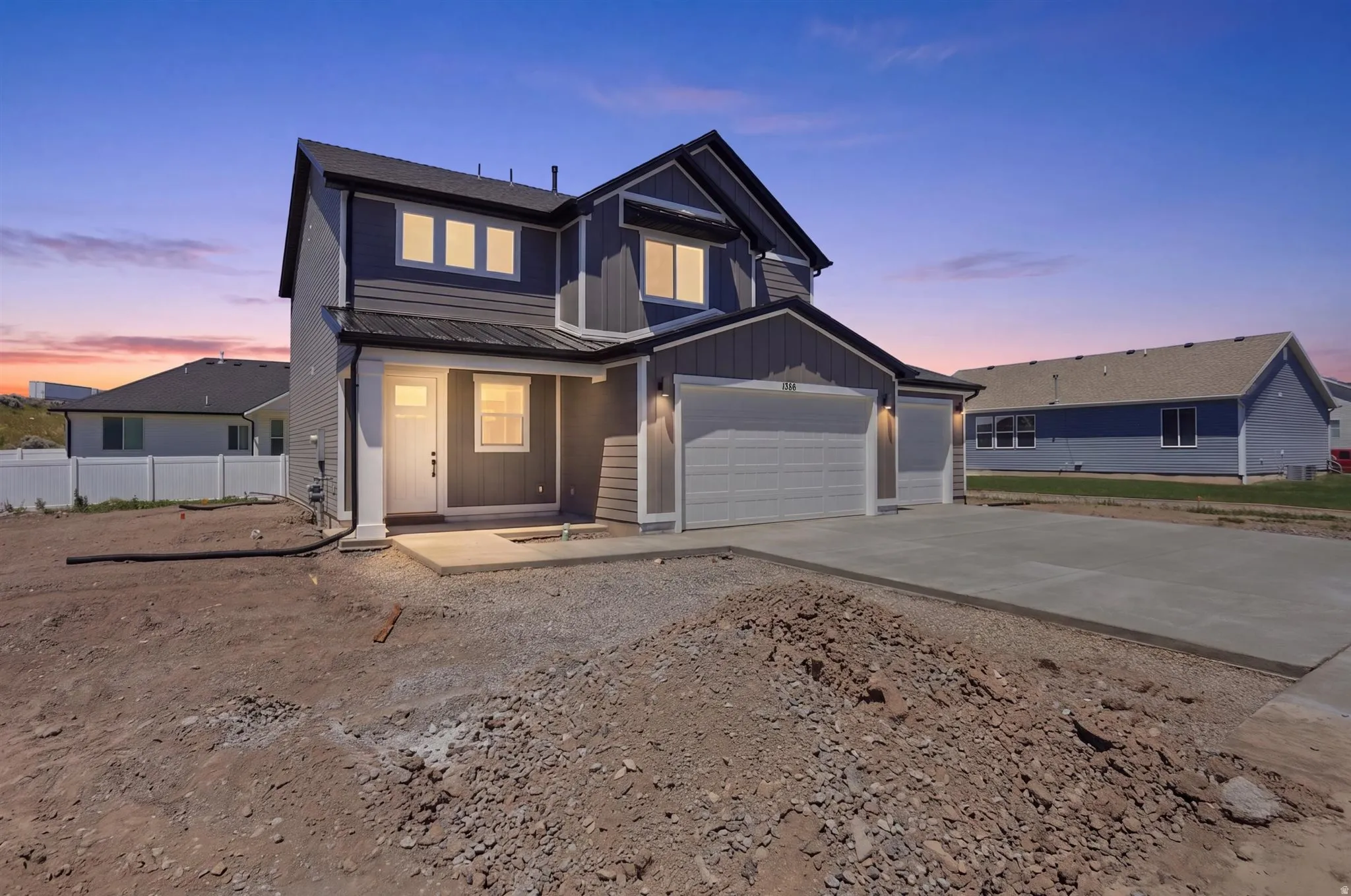 Contemporary exterior featuring dark gray siding with contrasting white trim, a covered entry porch, multiple window configurations, and an attached two-car garage with a concrete driveway