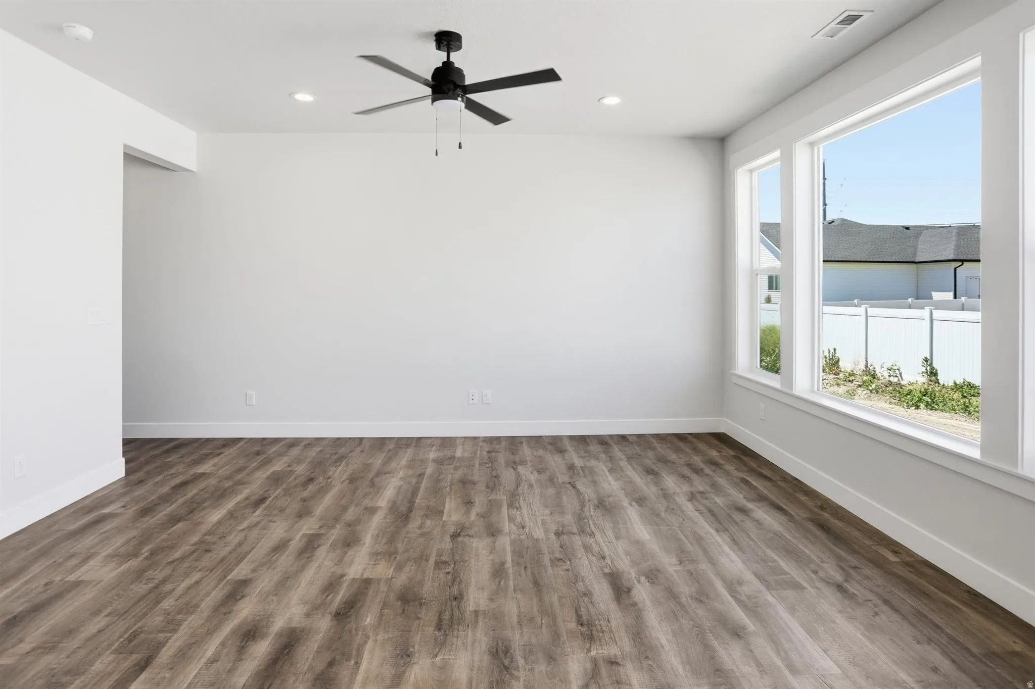 Spacious room with wood-finish flooring, white walls, and bright windows