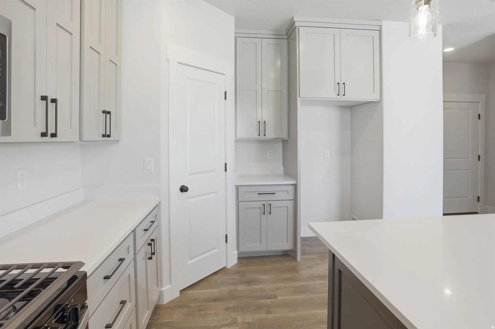Modern kitchen featuring light gray cabinetry with black hardware, white countertops, a built-in oven, and wood-finish flooring