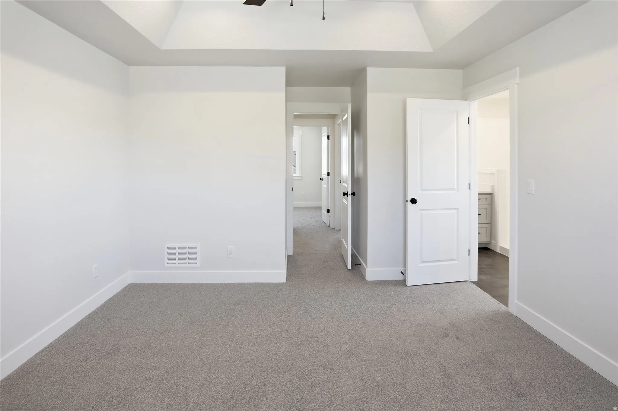 Spacious room with plush gray carpeting, white walls, and a tray ceiling