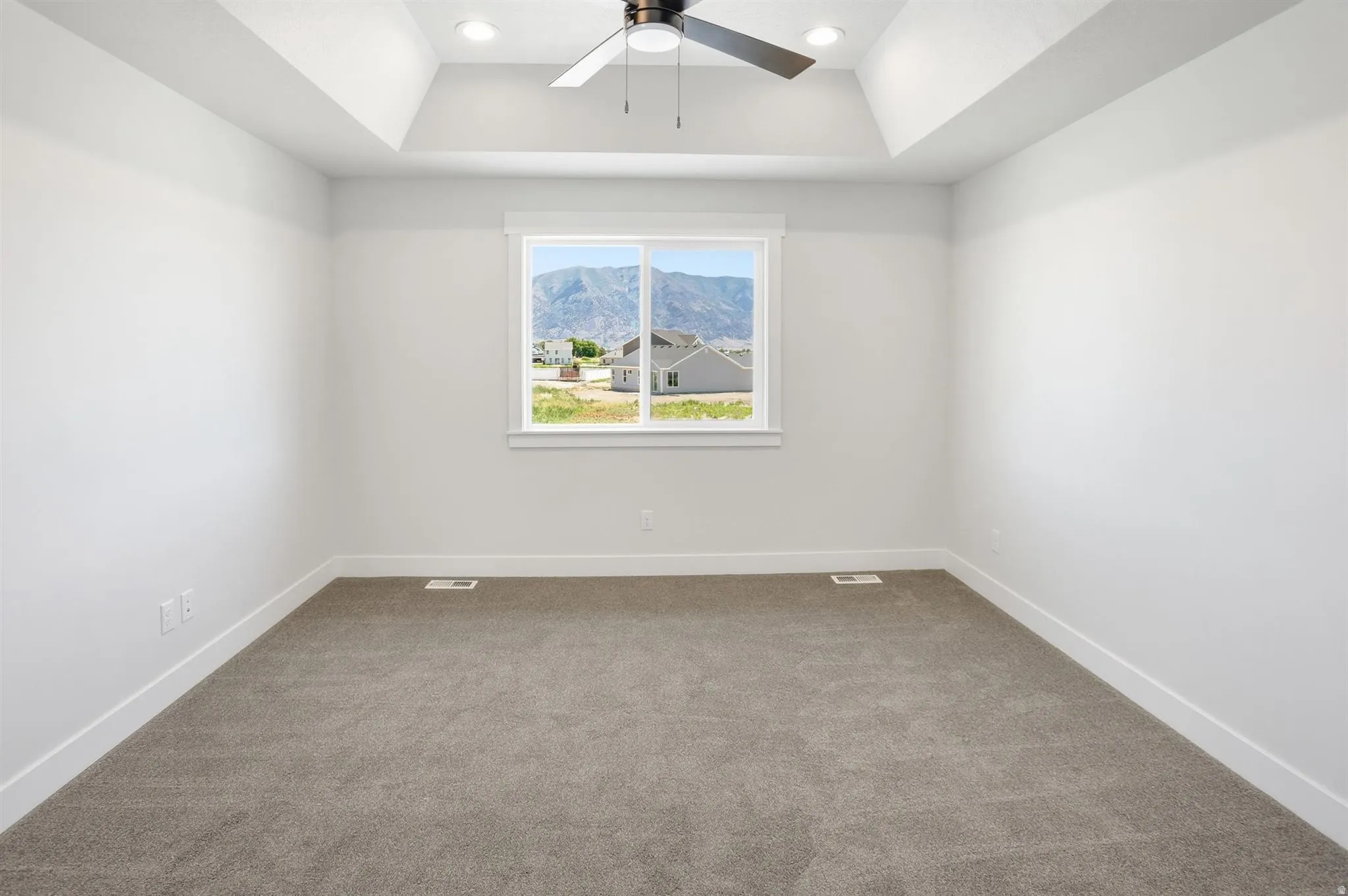 Spacious room featuring a tray ceiling with recessed lighting and ceiling fan