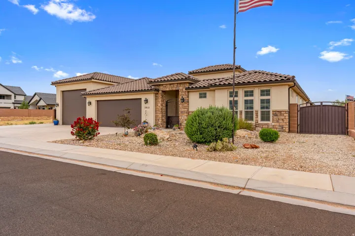 Stucco and stone exterior featuring a tile roof, two-car garage, and desert-style landscaping