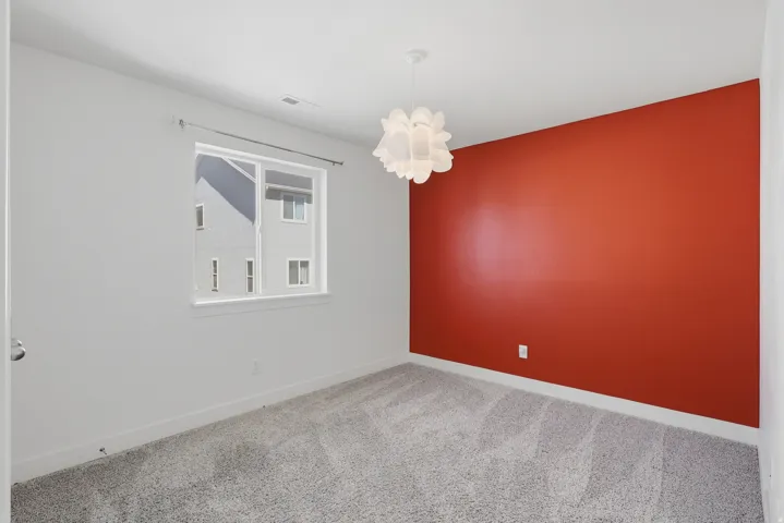 Bedroom featuring a vibrant accent wall, neutral carpeting, and a contemporary ceiling light fixture