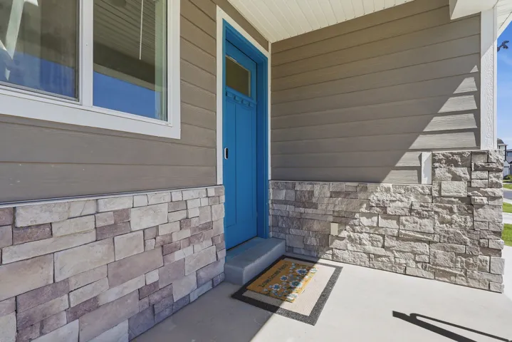 Front entry featuring a bright blue door, composite siding, and stone veneer accents