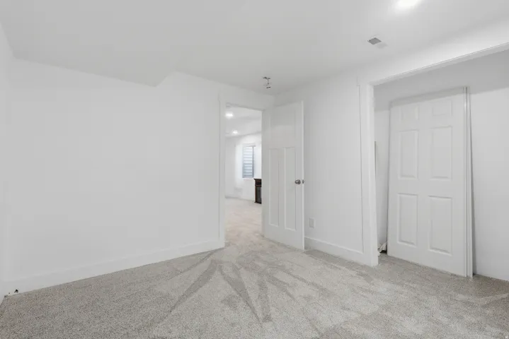 Carpeted room featuring white walls, white baseboards, a white paneled door, and a white six-panel bifold door