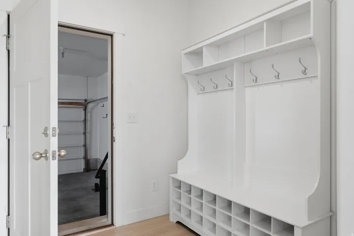 Built-in white storage unit featuring multiple hooks, open shelving, and individual shoe cubbies