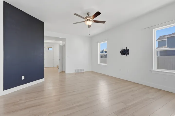 Spacious room featuring light wood-finish flooring, a ceiling fan with integrated lighting, and white trim throughout