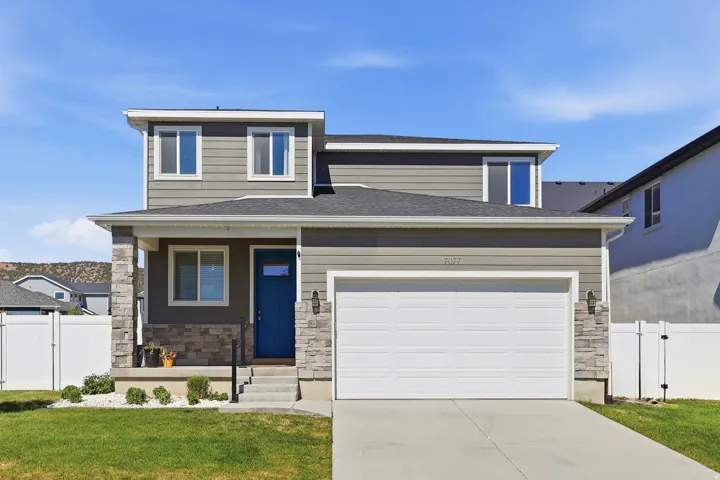 Two-story residence featuring gray siding, a prominent blue entry door, and stone facade accents