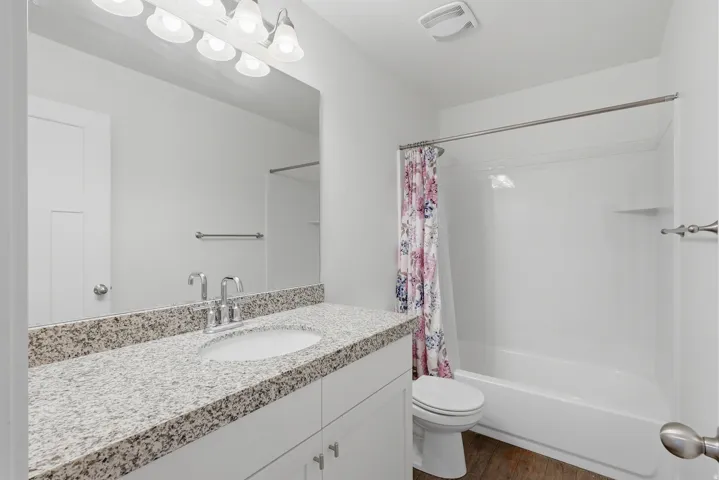 Bathroom featuring a white vanity with a speckled countertop, a large mirror, and a chrome light fixture