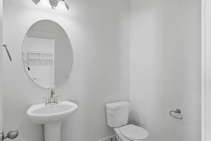 Pedestal sink with chrome faucet, an oval wall-mounted mirror, and a two-bulb vanity light fixture