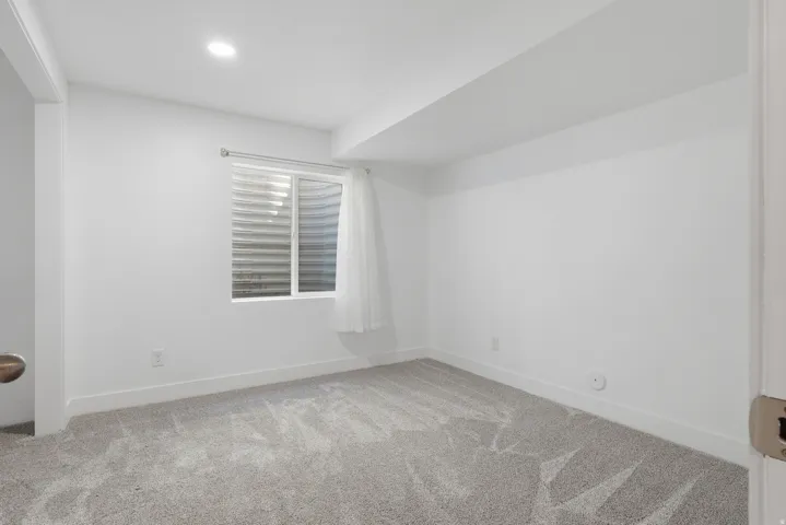 Recessed lighting illuminates a room featuring light gray carpet, white walls, and white baseboards