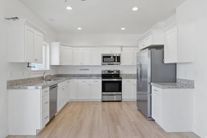 Bright kitchen featuring white shaker cabinetry, stainless steel appliances, speckled countertops, wood-finish flooring, and recessed lighting