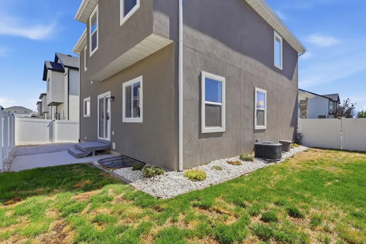 Modern stucco exterior with white-framed windows, a concrete patio, and a grass lawn