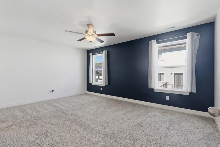 Spacious room featuring patterned carpet flooring, a ceiling fan with integrated lighting, and a contrasting accent wall with two windows