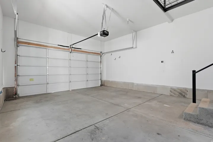 Spacious garage featuring a sectional overhead door, automatic opener, concrete flooring, and painted white walls