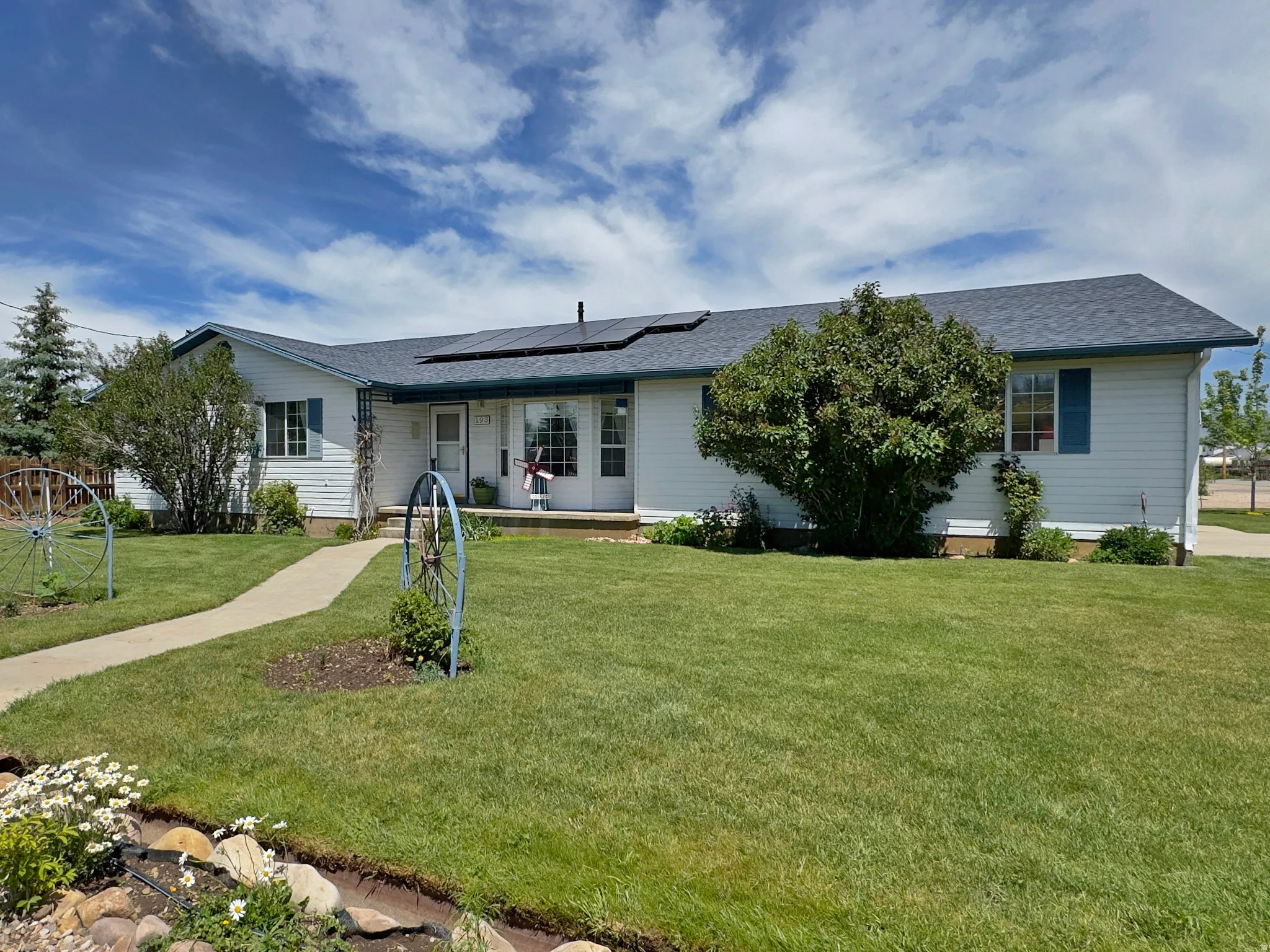 Single-story residence featuring white siding, a dark shingle roof with solar panels, and blue window shutters