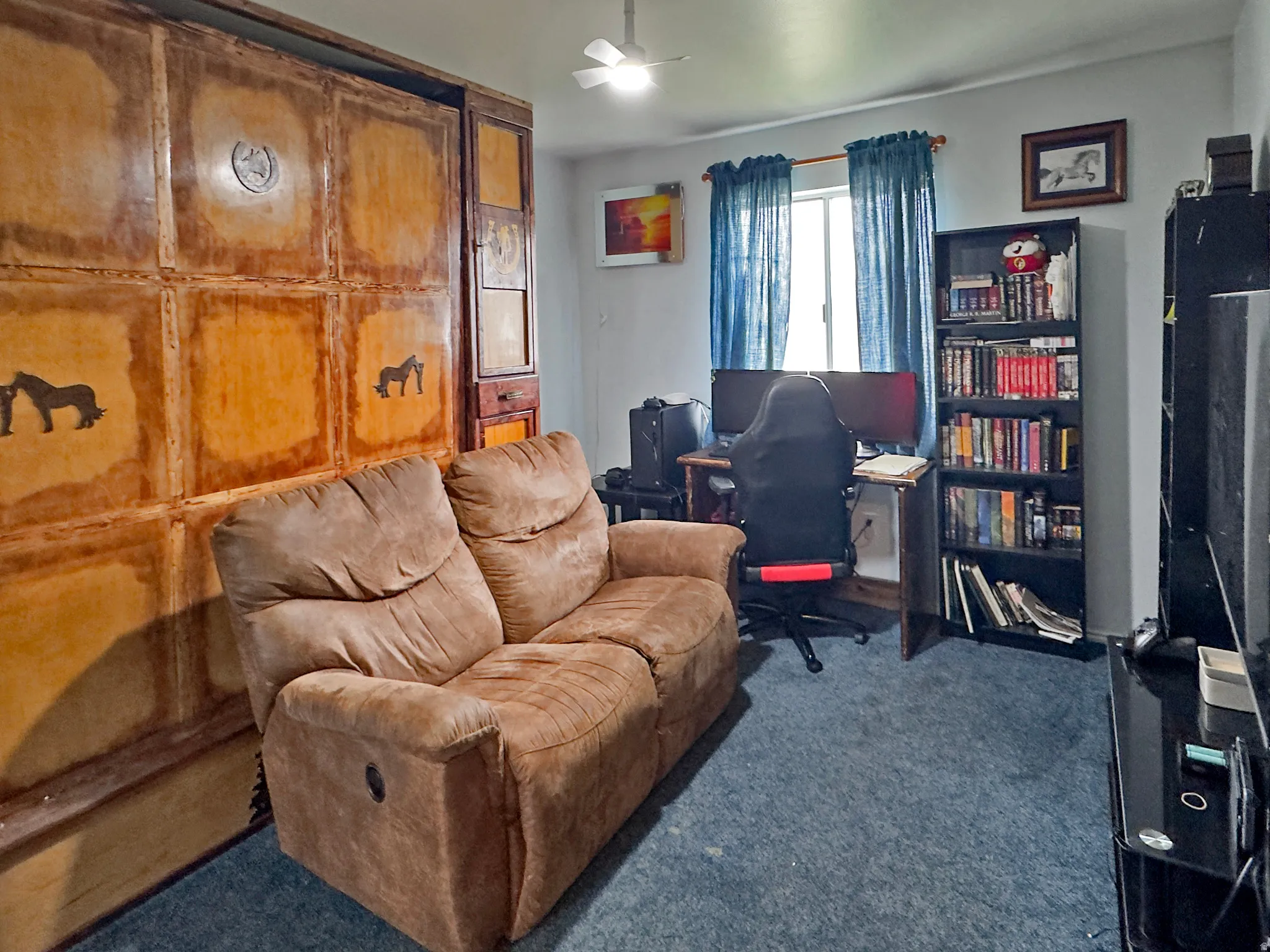 Room featuring a unique built-in wooden wall unit with decorative accents, blue carpeting, and a ceiling fan