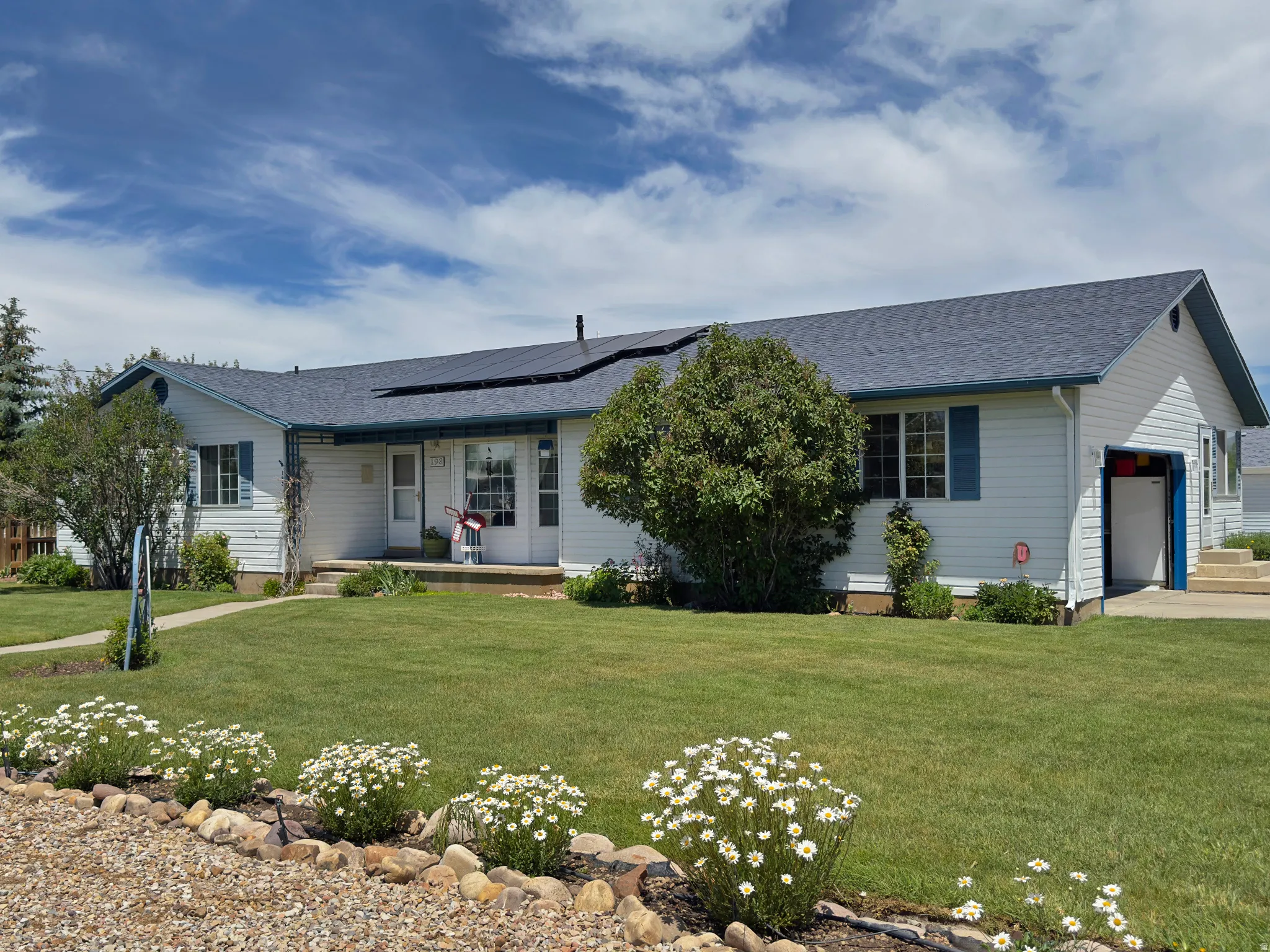 White siding residence featuring a dark shingled roof with solar panels