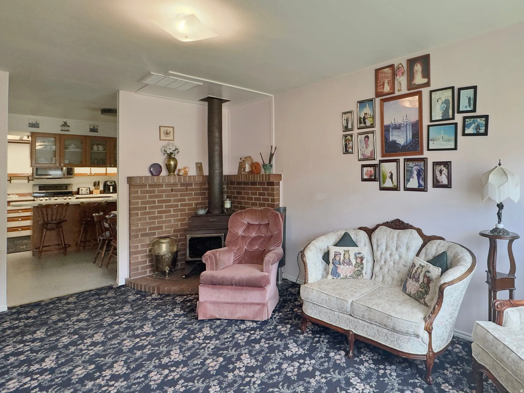 Living area featuring a brick hearth with a wood-burning stove, patterned carpeting, and a ceiling-mounted light fixture