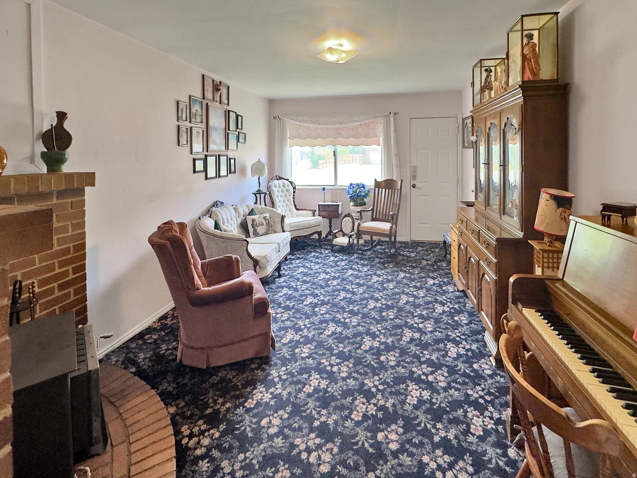 Spacious living area featuring a brick fireplace, patterned carpet flooring, a front entry door, and a large window with natural light