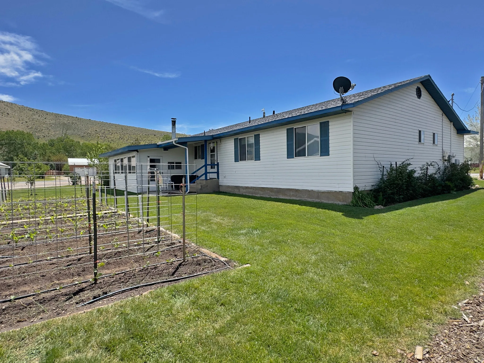 Spacious rear yard with a cultivated garden bed, extensive lawn, white vinyl siding, blue window shutters, and a covered back patio