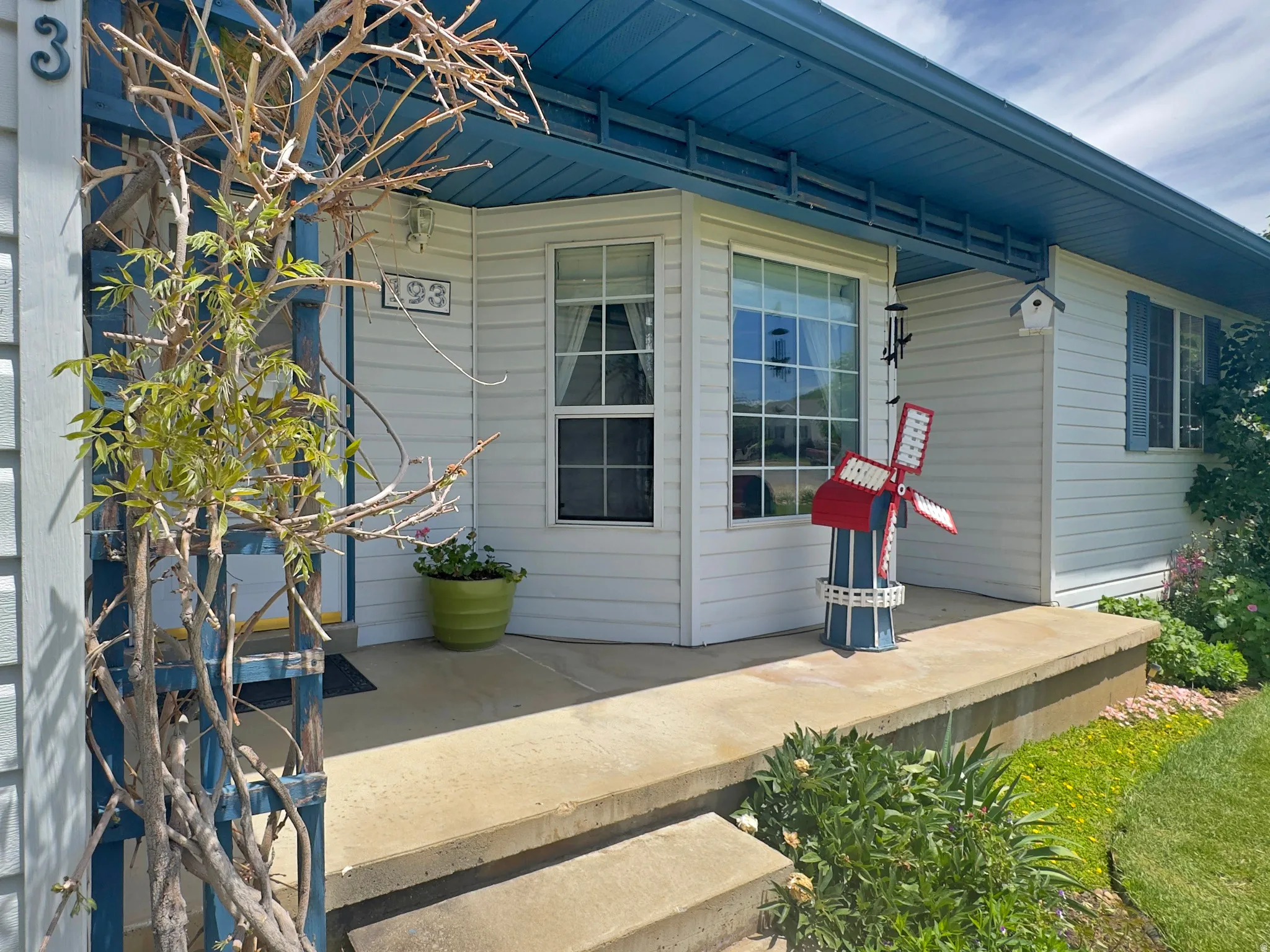 Covered front porch with concrete steps, featuring white siding and blue trim accents