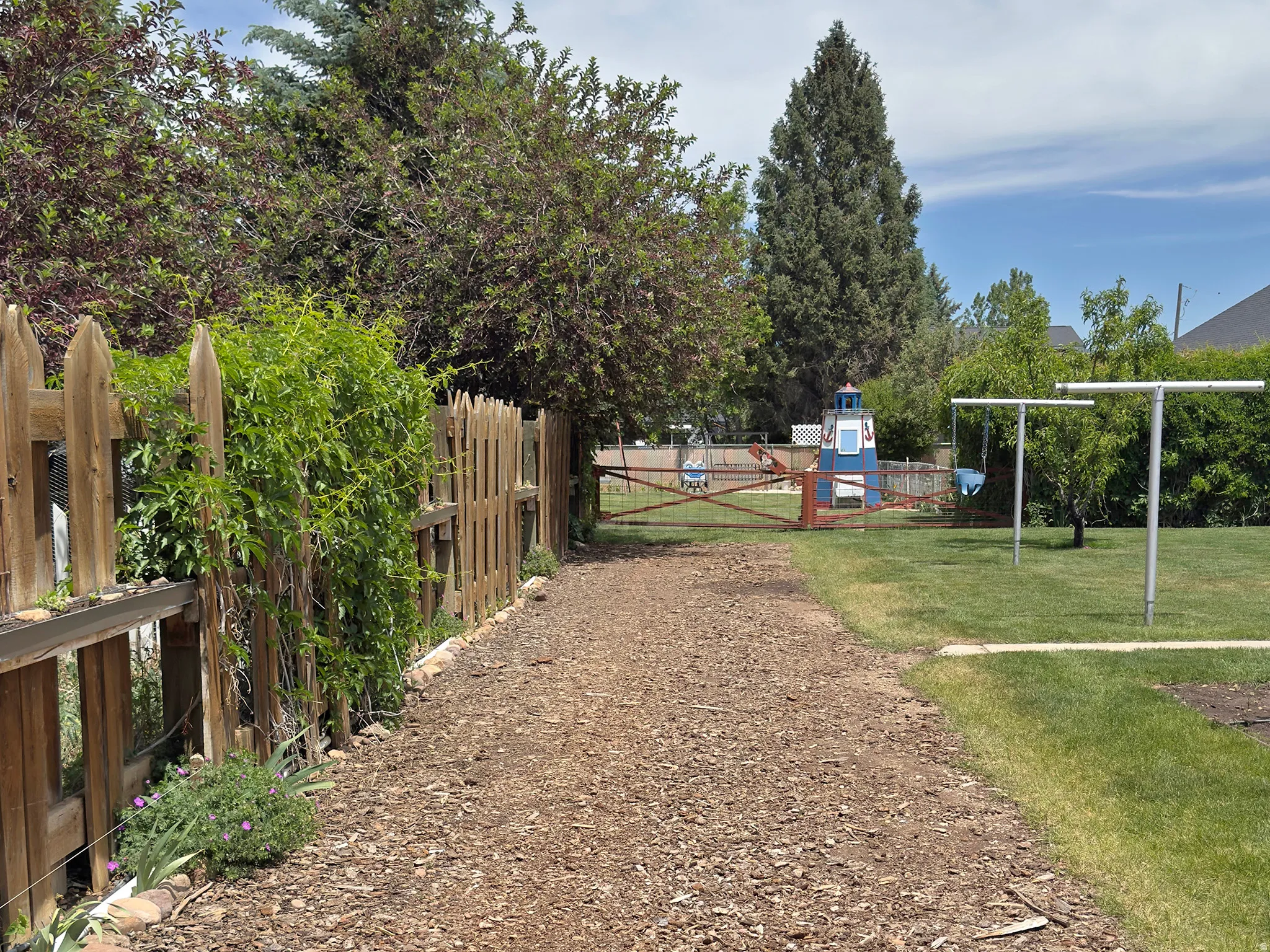 Expansive yard featuring a bark-mulch pathway, natural wood picket fencing, and a manicured lawn