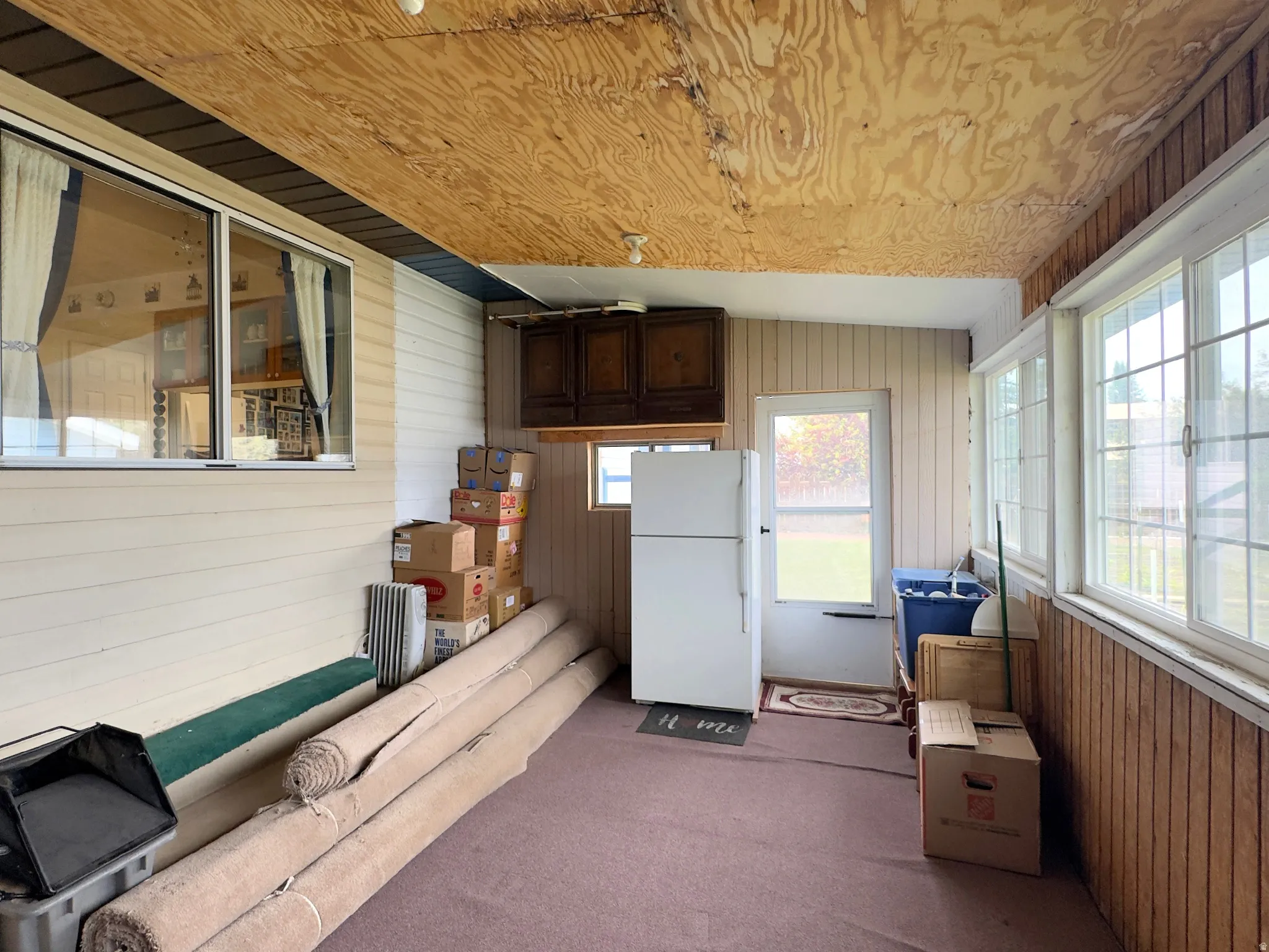 Enclosed porch featuring a wood panel ceiling, multiple windows, a white door, and built-in cabinetry