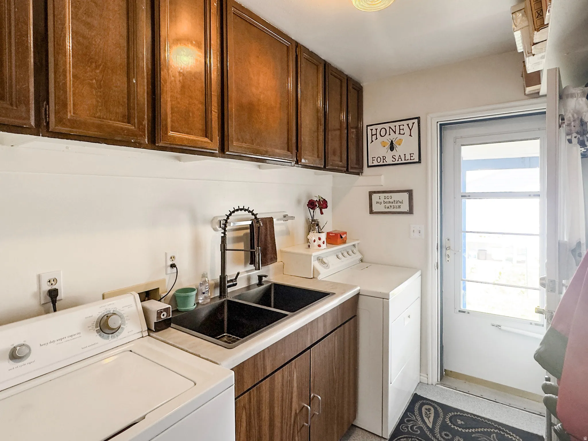 Utility room featuring wood-finish cabinetry, a double basin sink with a matte black faucet, and a white countertop