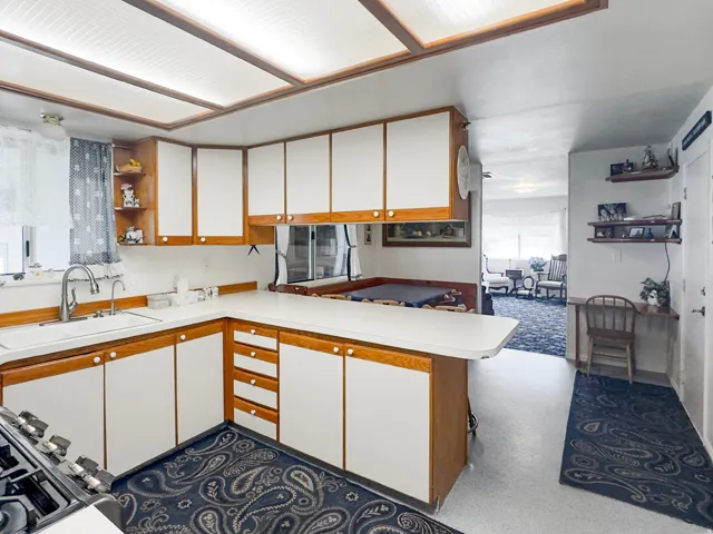 Kitchen featuring ample white cabinetry with wood-finish framing, white countertops, and a stainless steel sink with a gooseneck faucet